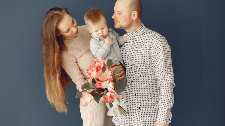 A joyful family moment with parents holding a child and a bouquet of pink flowers.