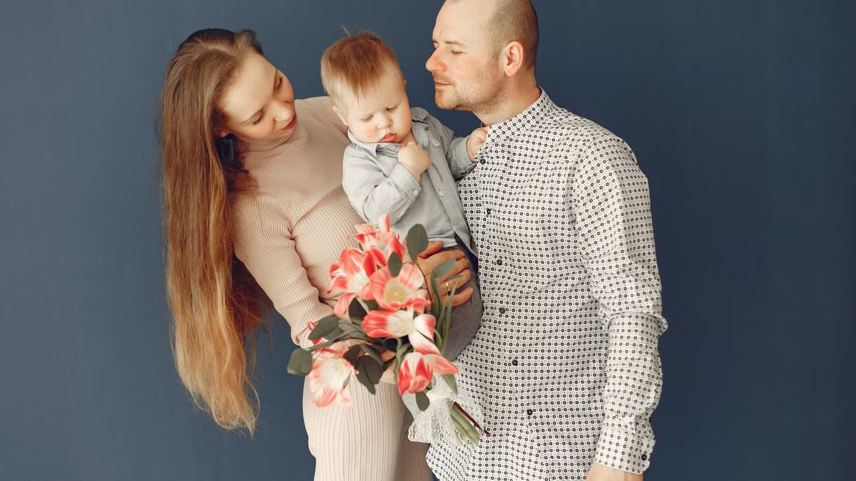A joyful family moment with parents holding a child and a bouquet of pink flowers.